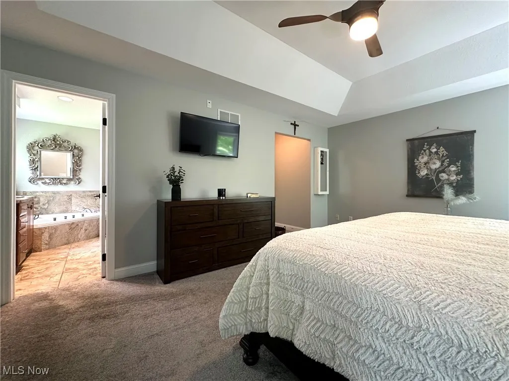Bedroom featuring light carpet, baseboards, ensuite bathroom, a ceiling fan, and vaulted ceiling