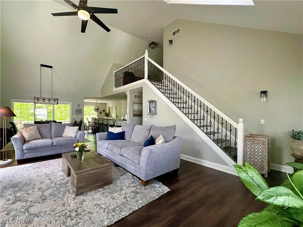 Living room with high vaulted ceiling, ceiling fan, wood finished floors, stairs, and baseboards