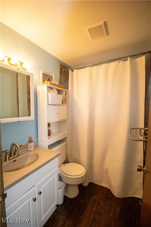 Bathroom featuring wood finished floors, vanity, toilet, and a shower with shower curtain