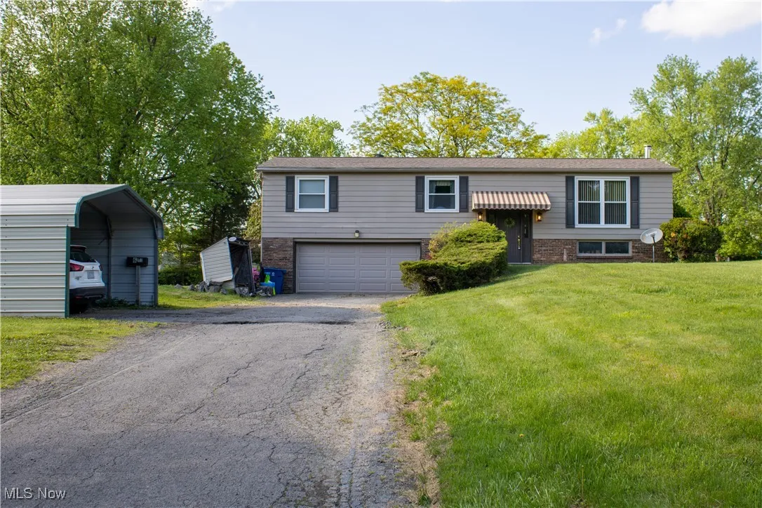 Raised ranch featuring driveway, a front yard, brick siding, a detached carport, and a garage