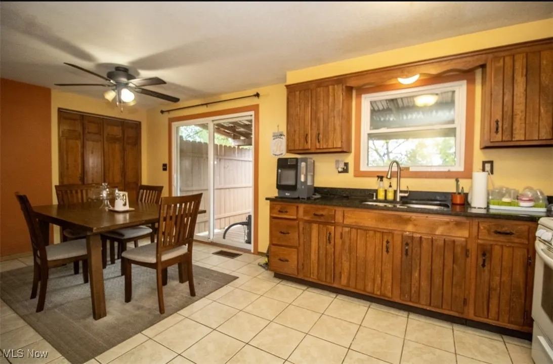 Kitchen with a sink, brown cabinets, ceiling fan, dark countertops, and light tile patterned floors