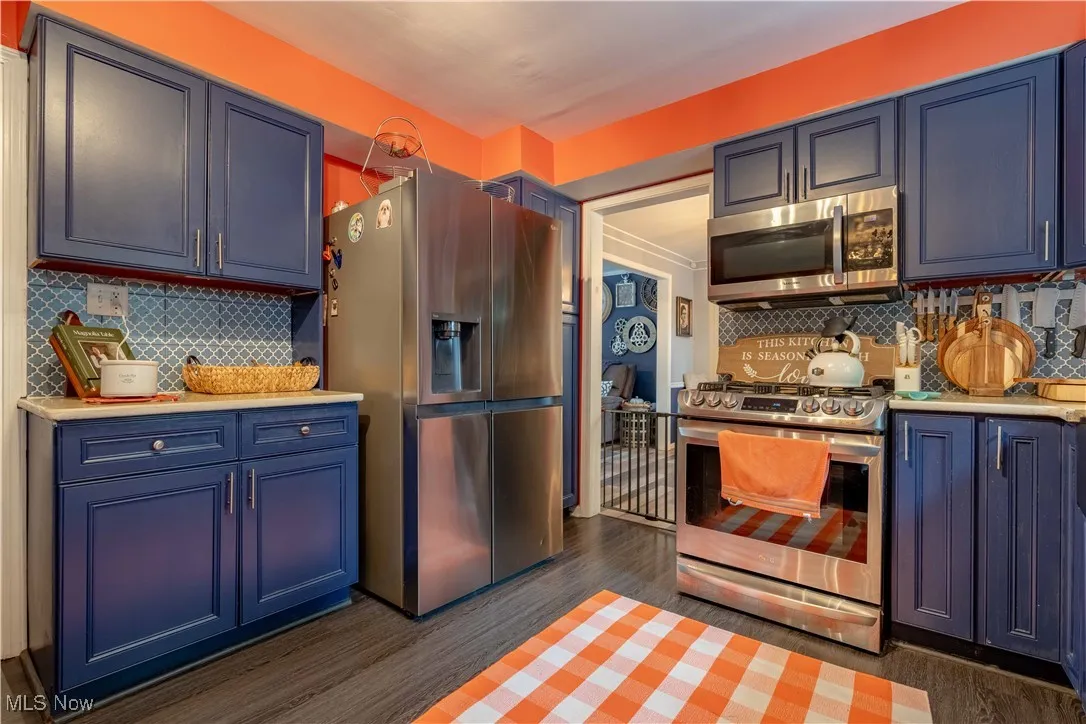 Kitchen featuring stainless steel appliances, light countertops, blue cabinets, and tasteful backsplash