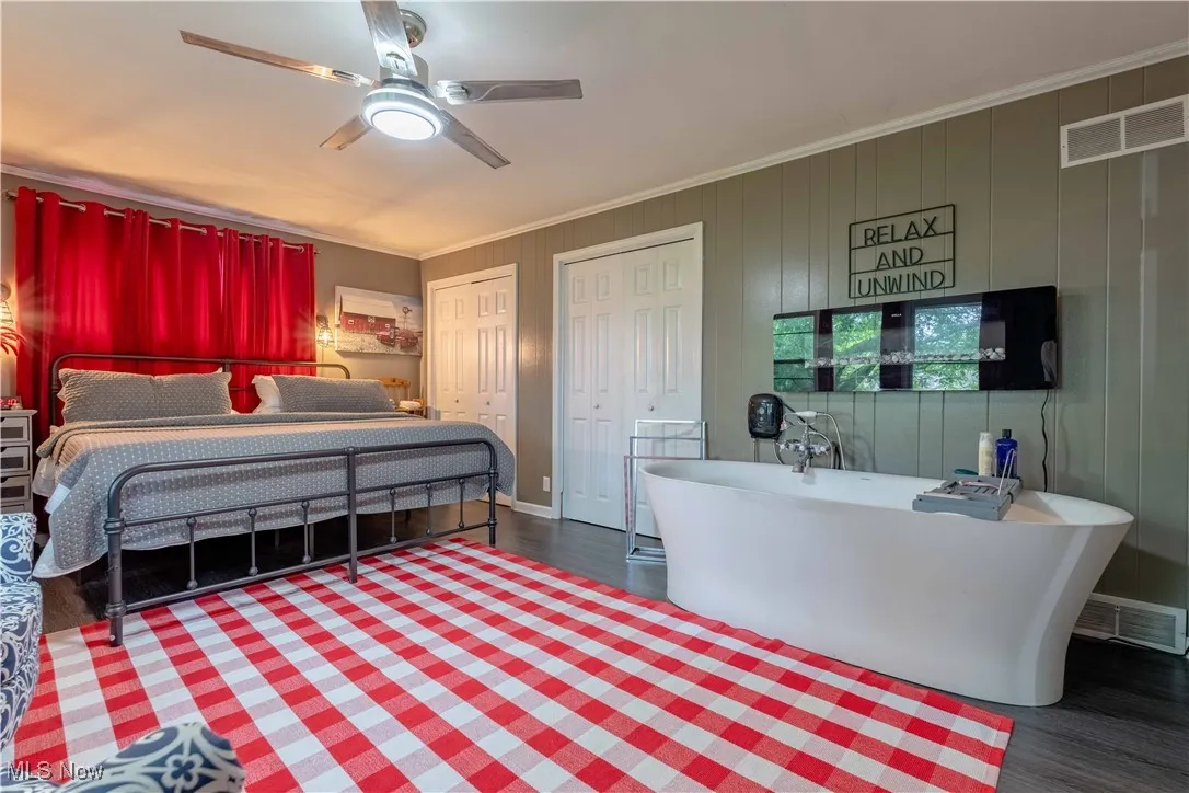 Bedroom featuring two closets, wood finished floors, ornamental molding, and ceiling fan