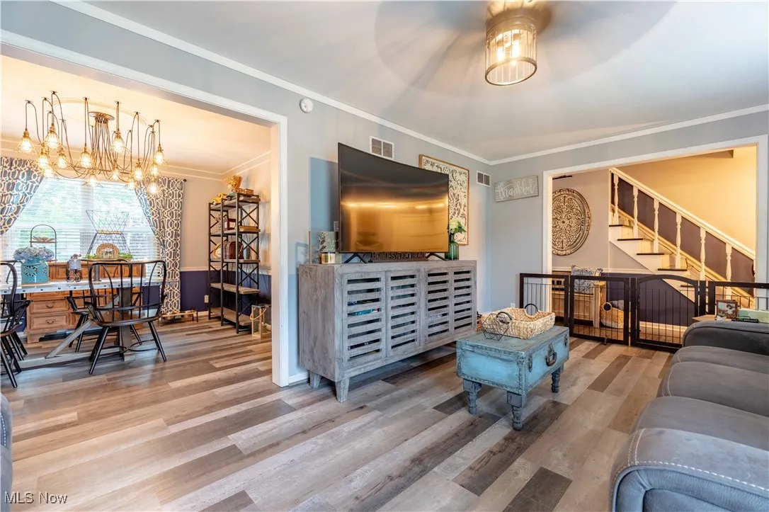 Living room with wood finished floors, a chandelier, ornamental molding, stairs, and baseboards