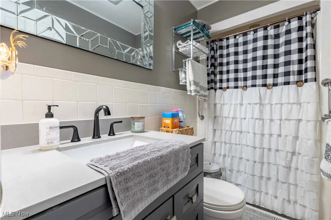 Full bath featuring toilet, a shower with curtain, tile walls, and vanity