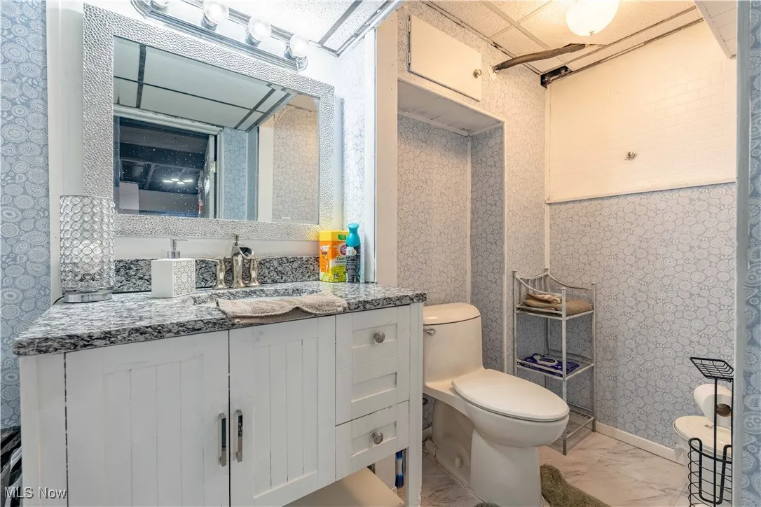 Bathroom with toilet, marble finish flooring, wallpapered walls, and vanity