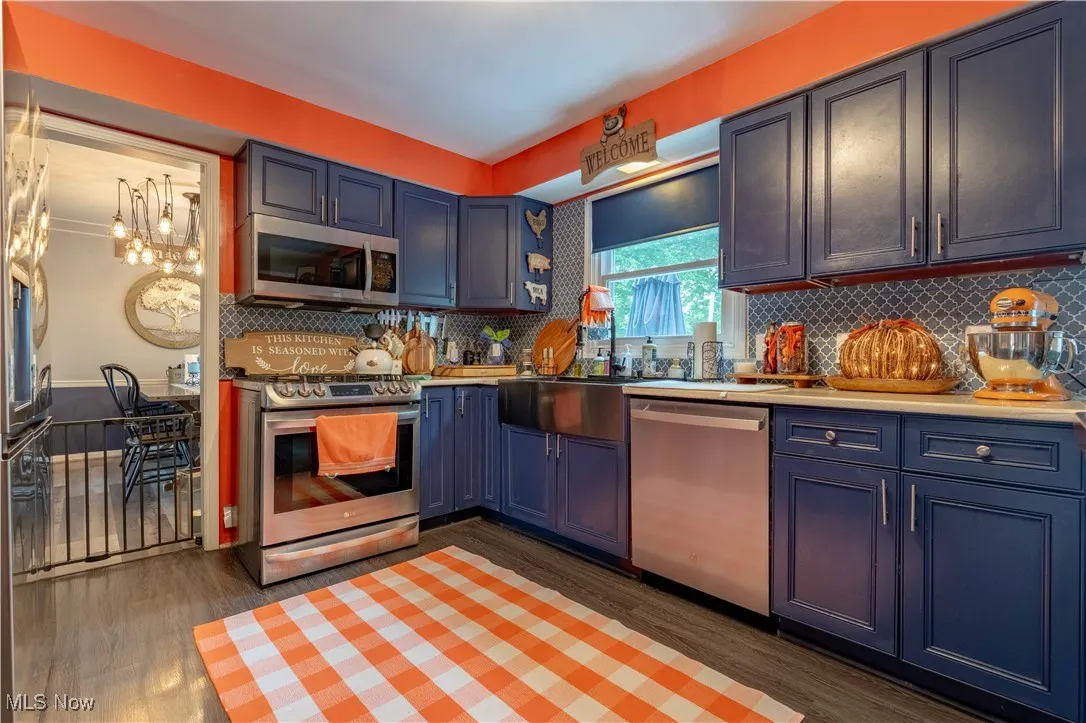 Kitchen featuring appliances with stainless steel finishes, wood finished floors, blue cabinets, and backsplash