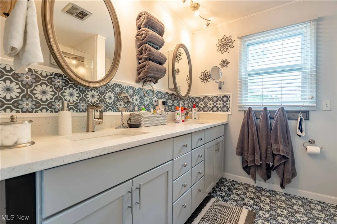 Bathroom featuring double vanity, ornamental molding, and decorative backsplash