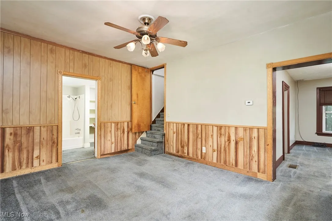 Living room featuring wood walls, a ceiling fan, stairs, carpet, and baseboards