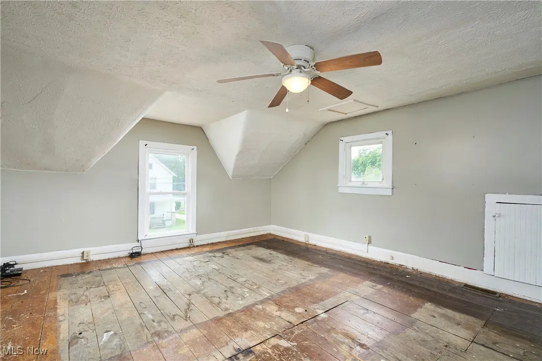 Additional living space with hardwood / wood-style flooring, a textured ceiling, baseboards, lofted ceiling, and ceiling fan