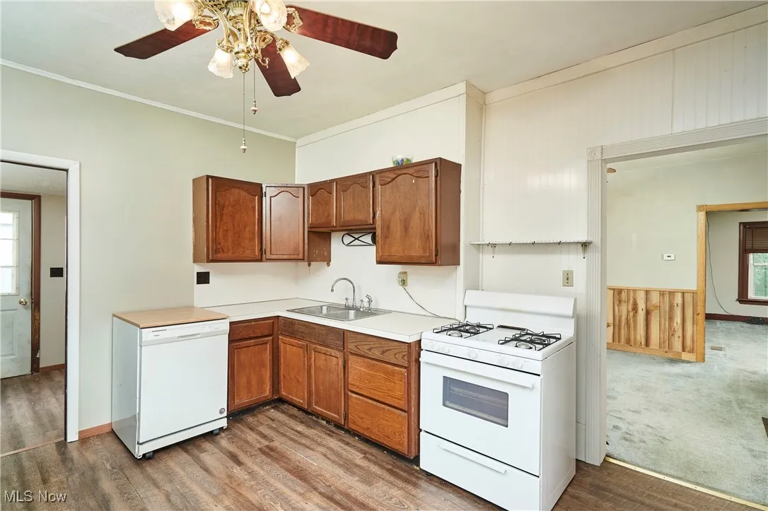 Kitchen featuring white appliances, a sink, ceiling fan, wood finished floors, and crown molding