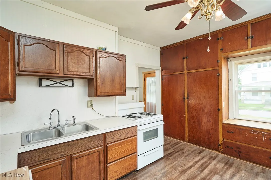 Kitchen with gas range gas stove, a sink, ceiling fan, light countertops, and wood finished floors