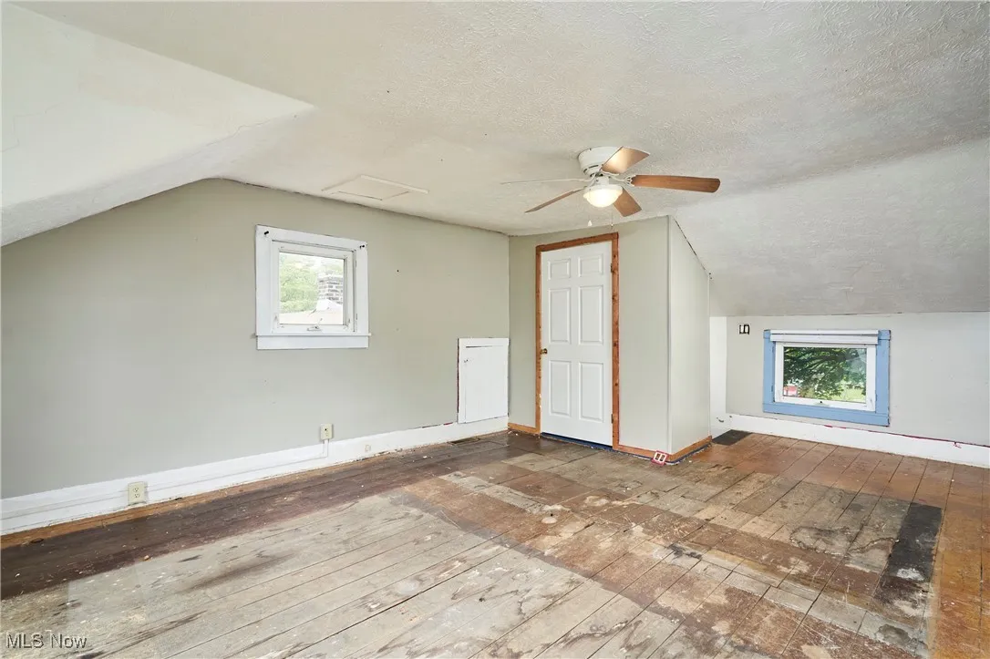 Bonus room featuring hardwood / wood-style flooring, lofted ceiling, baseboards, a textured ceiling, and a ceiling fan