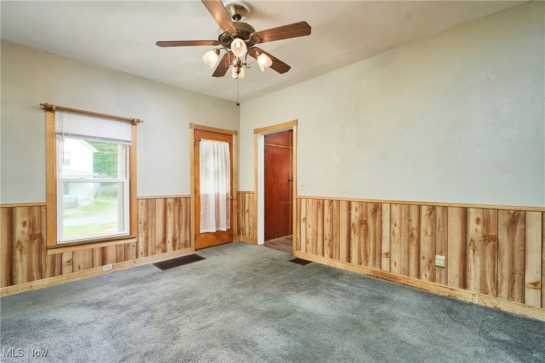 Living room featuring wainscoting, wood walls, carpet flooring, and a ceiling fan