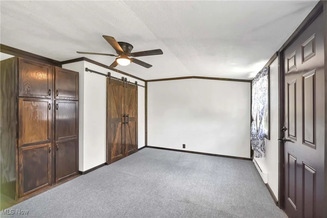 Unfurnished bedroom with ornamental molding, baseboards, carpet floors, a barn door, and a ceiling fan