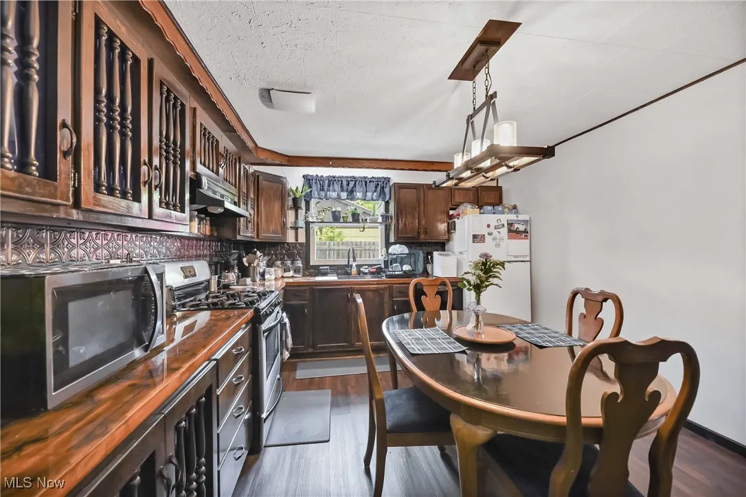 Kitchen featuring stainless steel appliances, under cabinet range hood, dark countertops, dark wood finished floors, and a textured ceiling