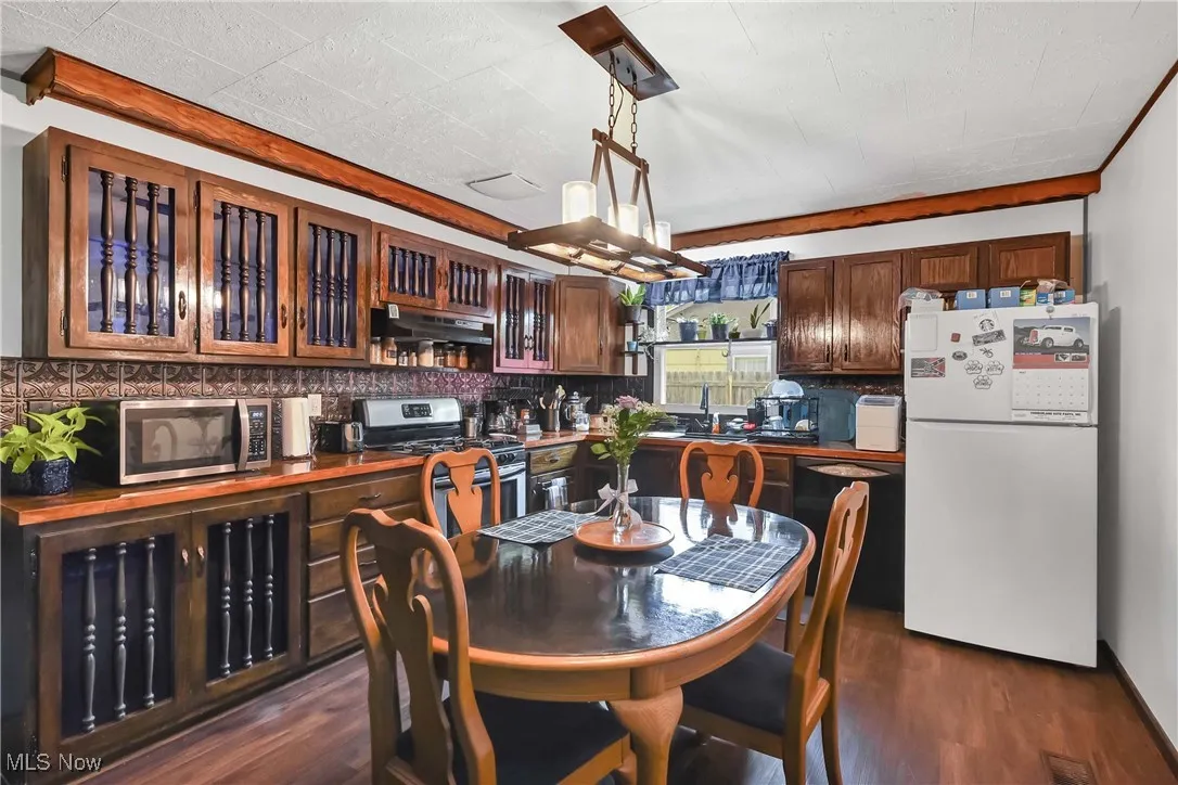 Kitchen with stainless steel appliances, under cabinet range hood, dark wood finished floors, and backsplash