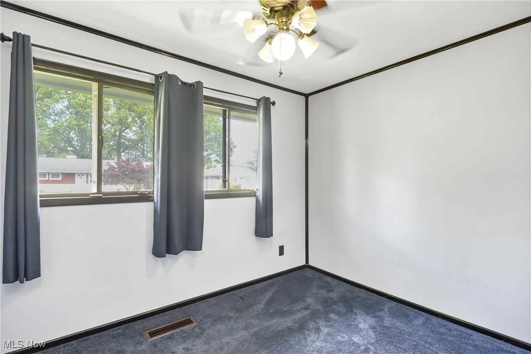 Empty room with dark colored carpet, ceiling fan, and baseboards
