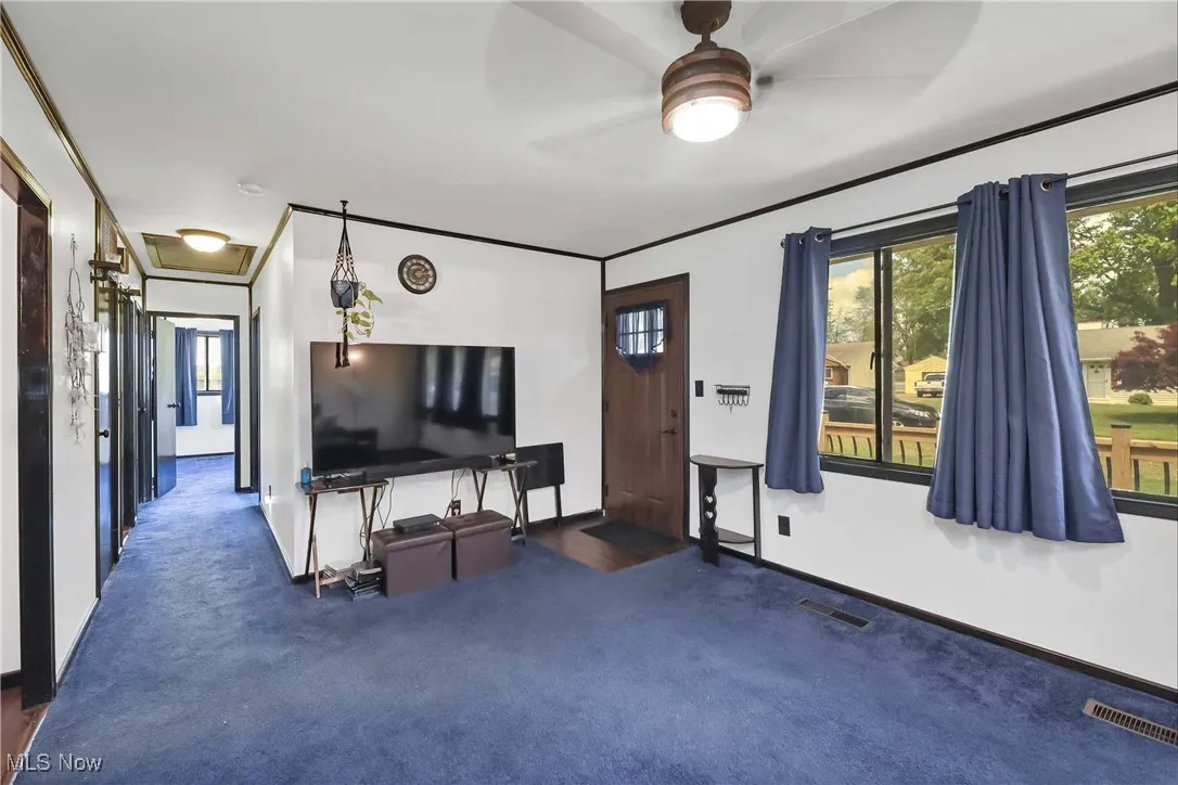 Carpeted living room featuring a ceiling fan and baseboards