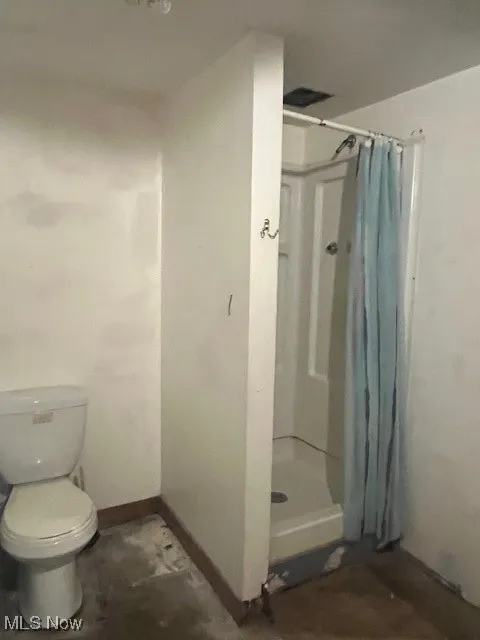 Bathroom featuring a stall shower, baseboards, and toilet