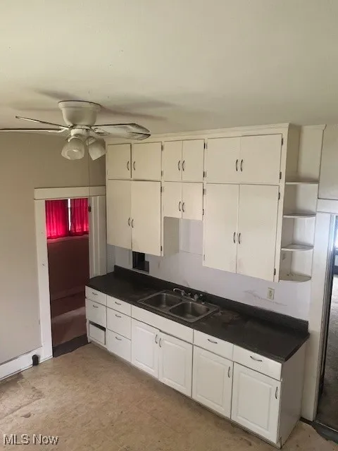 Kitchen featuring a sink, open shelves, dark countertops, and ceiling fan