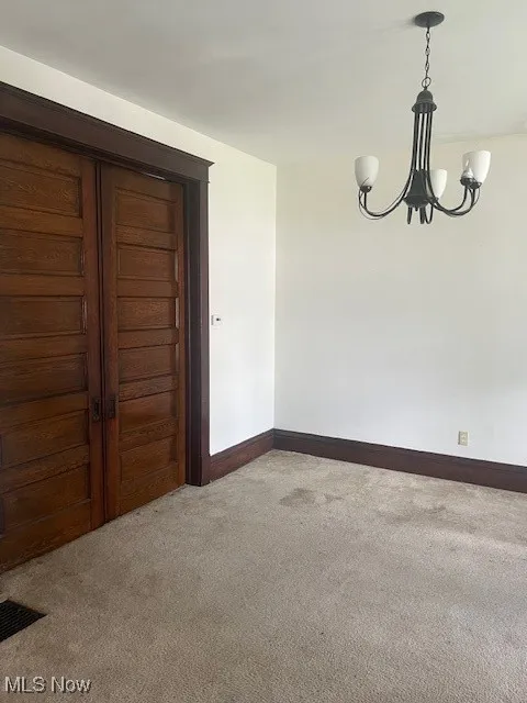 Empty room featuring light colored carpet, a chandelier, and baseboards