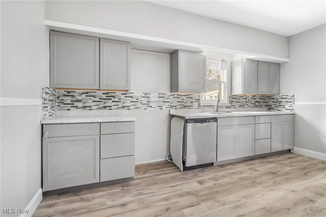 Kitchen with gray cabinetry, stainless steel dishwasher, light countertops, and a sink