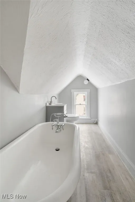Full bathroom with lofted ceiling, a textured ceiling, a freestanding bath, and baseboards