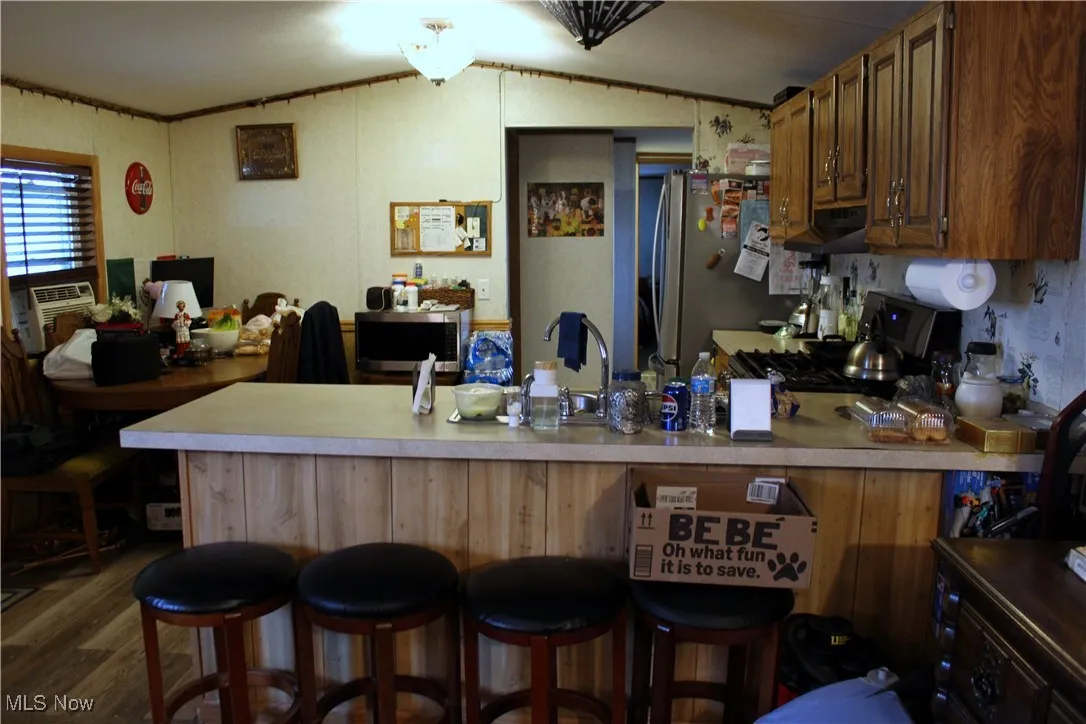 Kitchen featuring stainless steel appliances, lofted ceiling, a peninsula, wood finished floors, and light countertops