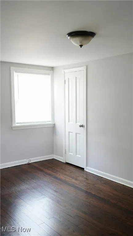 Spare room featuring dark wood-style flooring and baseboards
