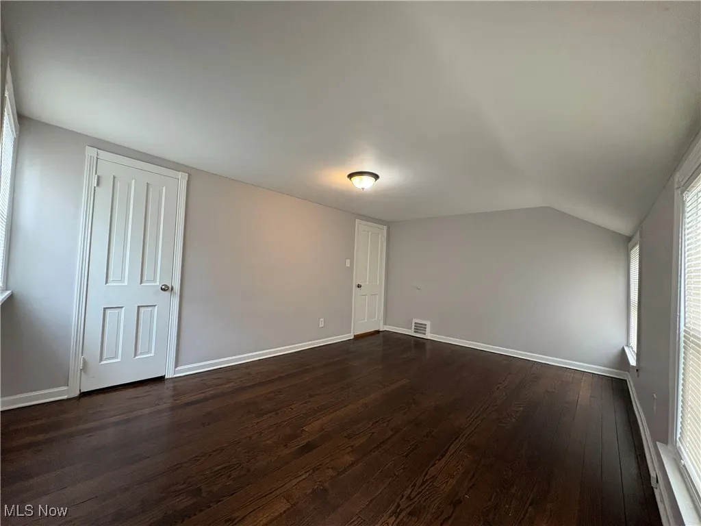 Unfurnished room featuring dark wood-style flooring, lofted ceiling, and baseboards