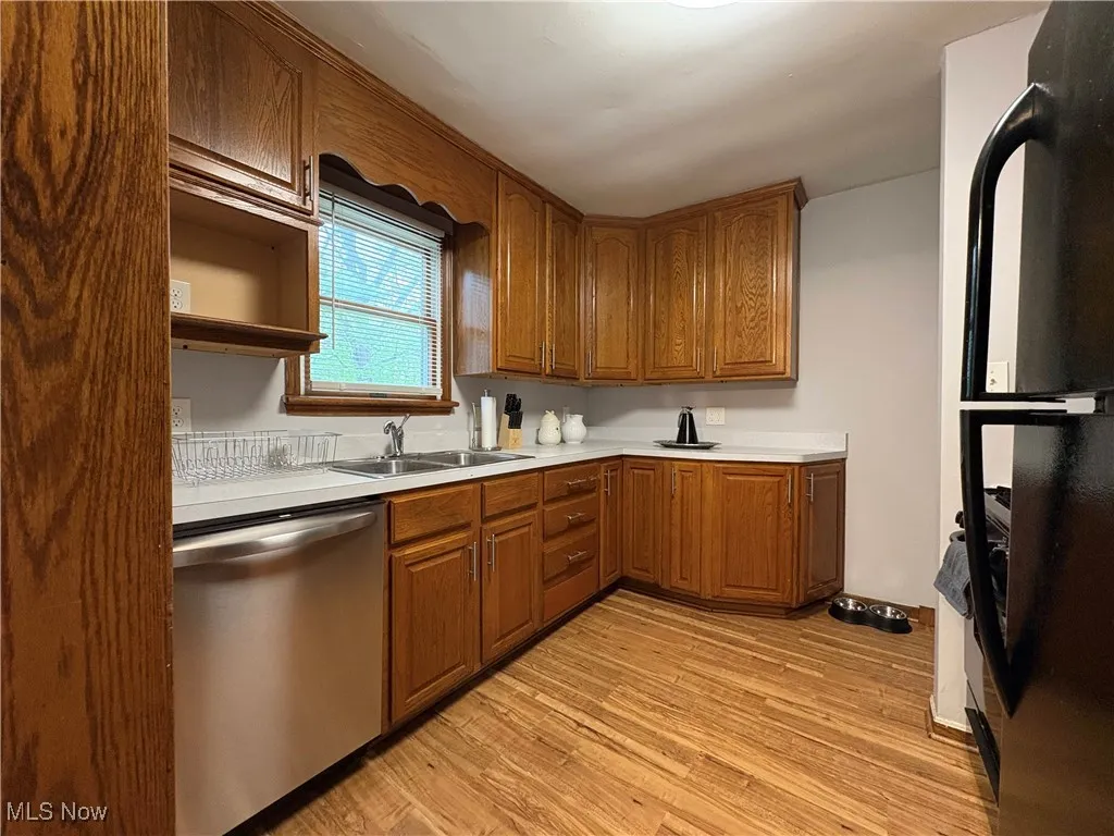 Kitchen with stainless steel dishwasher, freestanding refrigerator, a sink, light countertops, and light wood-style floors