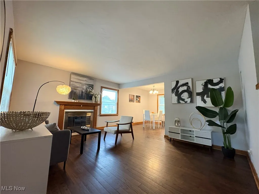 Living room with dark wood finished floors, a chandelier, a glass covered fireplace, and baseboards