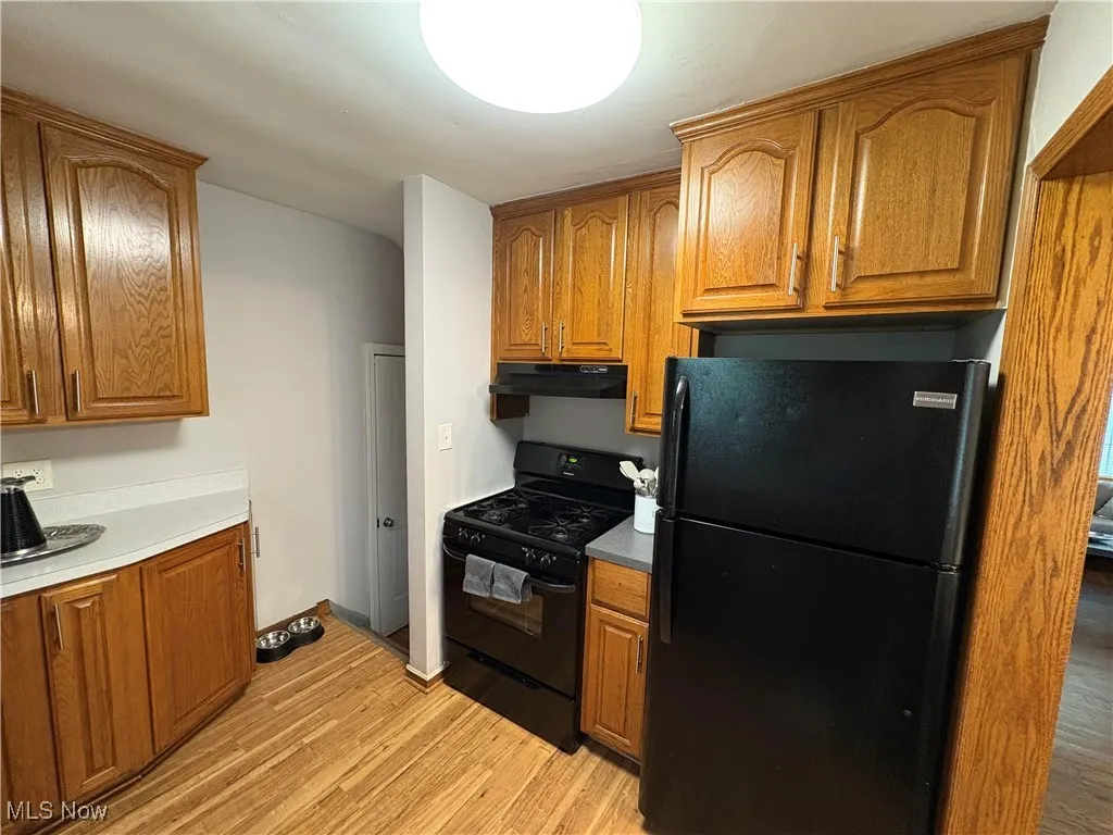 Kitchen featuring black appliances, under cabinet range hood, brown cabinets, and light wood-type flooring