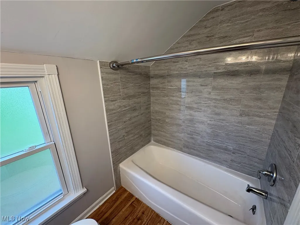 Full bath with shower / bathtub combination, wood finished floors, and vaulted ceiling