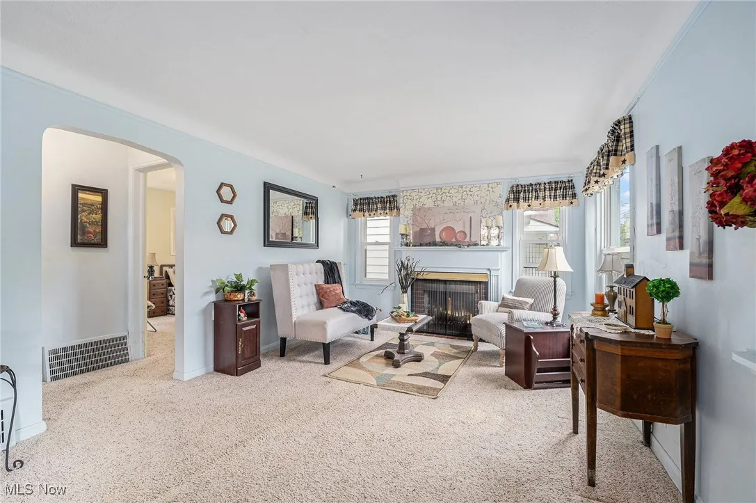 Living room with arched walkways, carpet, and a warm lit fireplace