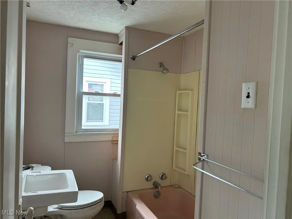 Full bath with a textured ceiling, bathing tub / shower combination, and toilet