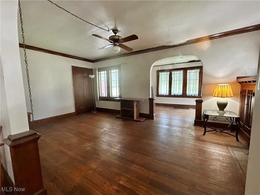 Living room featuring arched walkways, crown molding, wood floors, baseboards, and ceiling fan