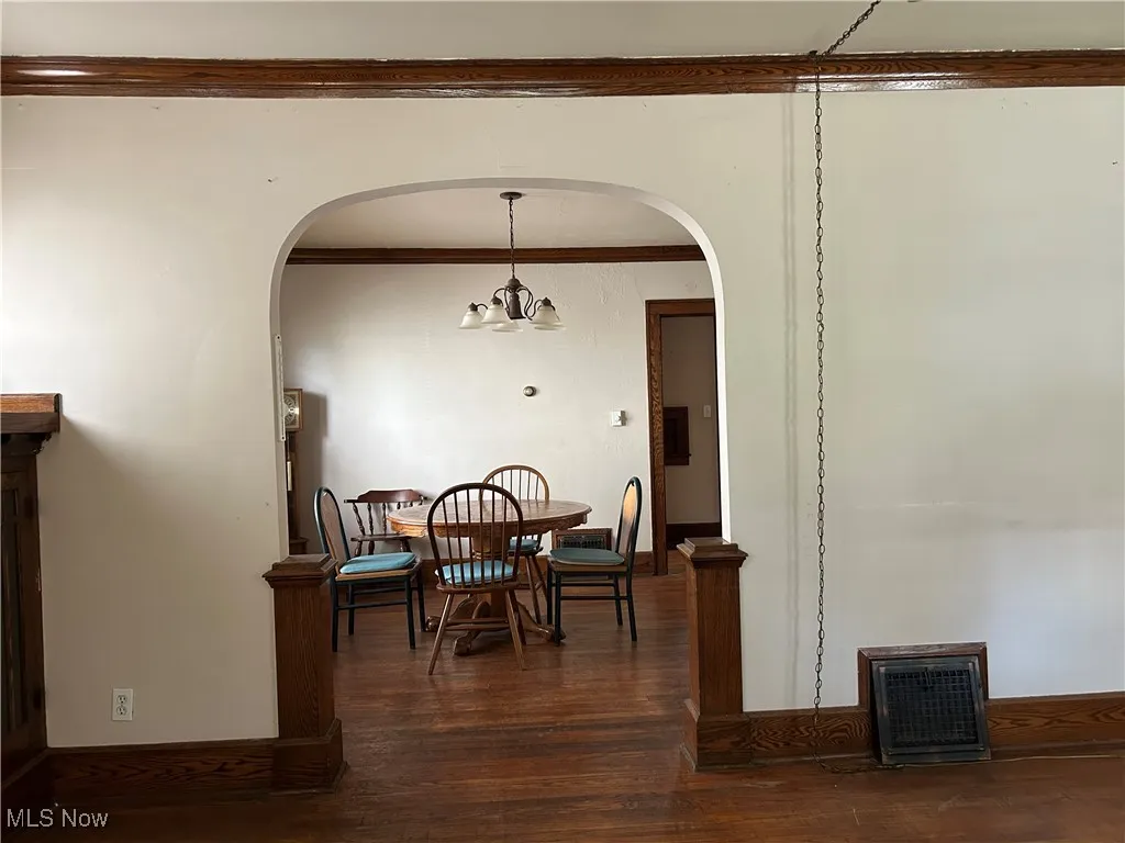 Dining area with arched walkways, dark wood-style floors, a chandelier, and crown molding