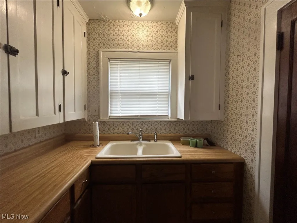 First Floor Kitchen featuring wallpapered walls, a sink, white cabinetry, and light countertops