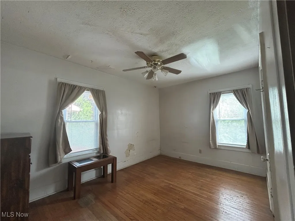  First floor apartment bedroom with plenty of natural light, wood flooring, a ceiling fan, a textured ceiling, and baseboards
