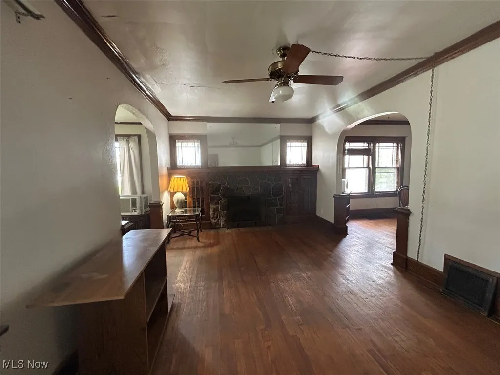 Living room featuring a fireplace, arched walkways, ornamental molding, dark wood floors, and ceiling fan