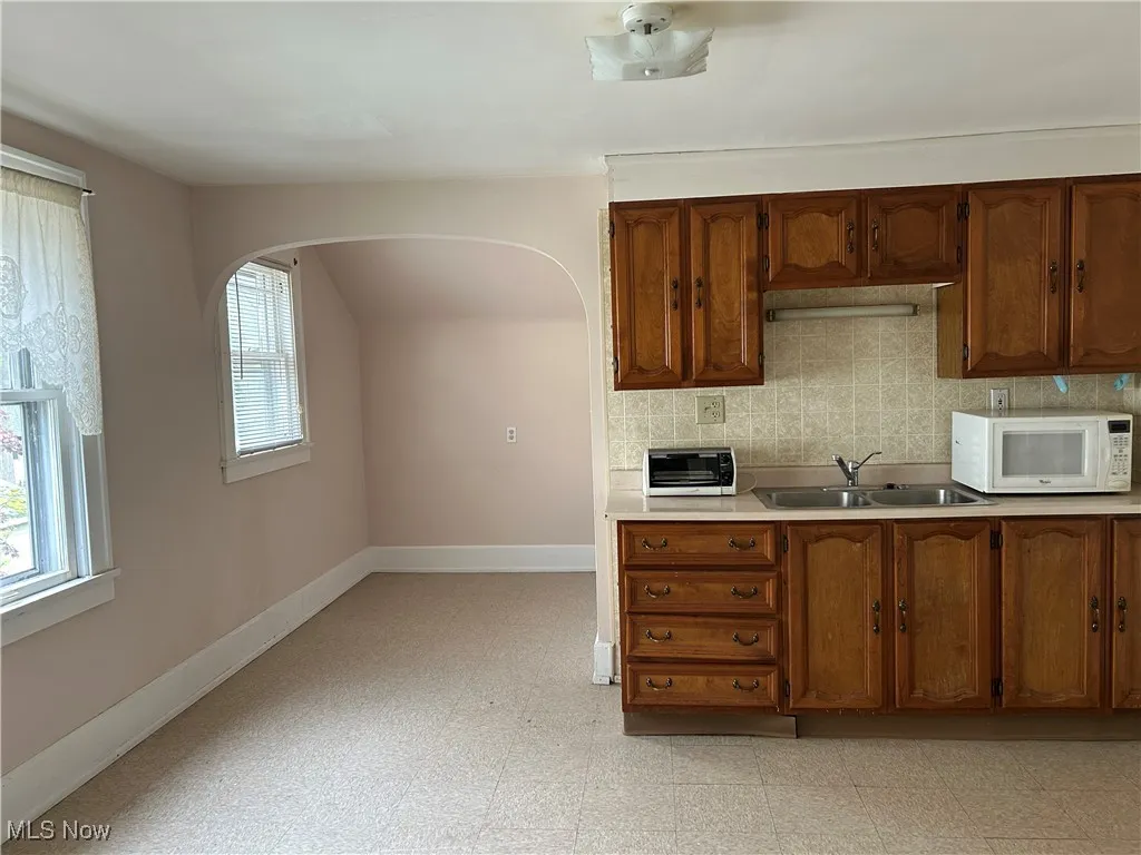 Kitchen with a sink, baseboards, arched walkways, and light countertops