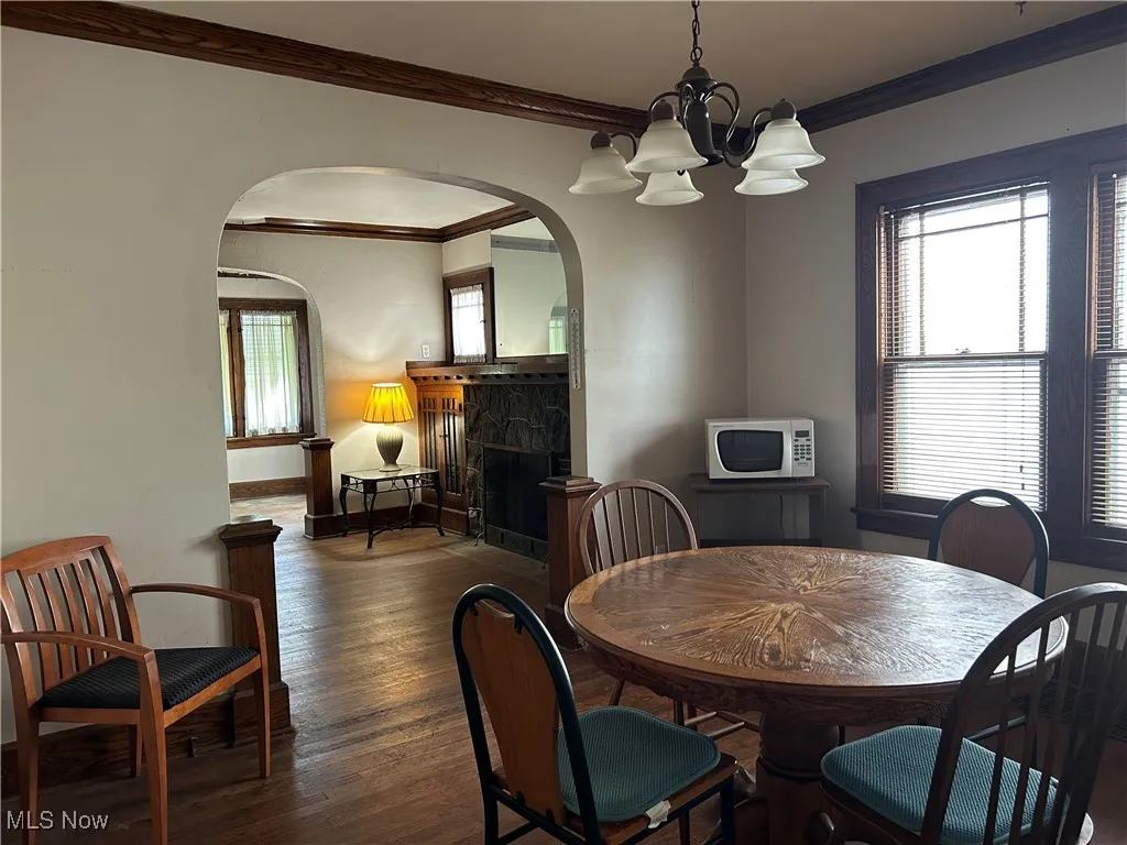 Dining area with arched walkways, crown molding, a chandelier, wood finished floors, and a fireplace