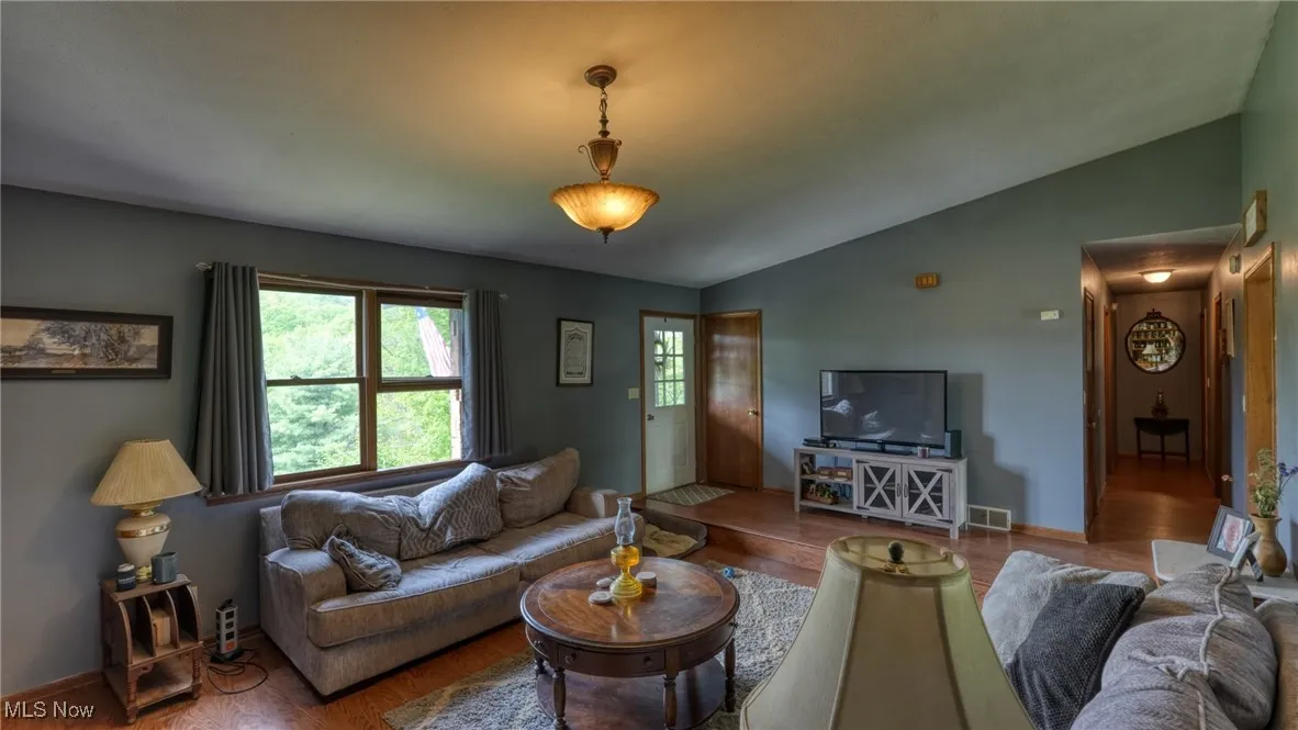 Living area with vaulted ceiling, wood finished floors, and baseboards
