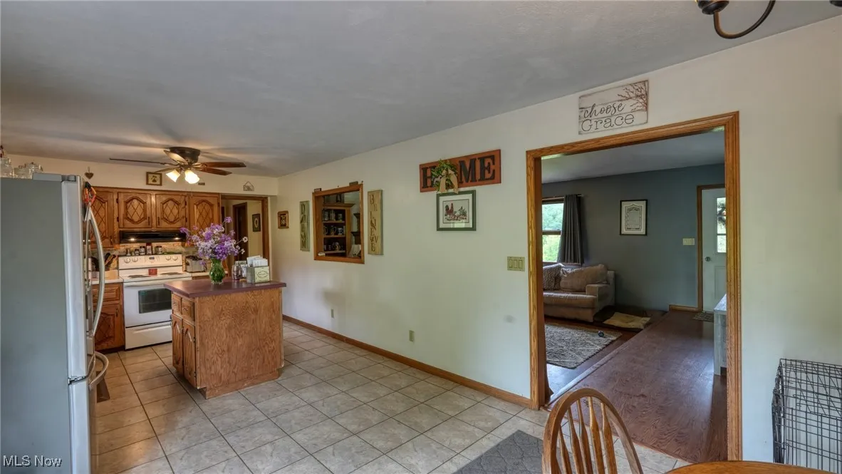 Kitchen with freestanding refrigerator, white range with electric stovetop, a kitchen island, ceiling fan, and brown cabinets