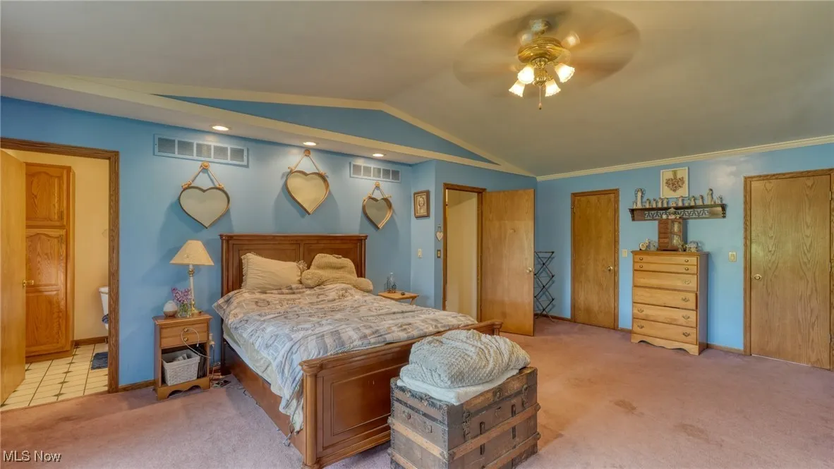 Bedroom featuring carpet flooring, lofted ceiling, ensuite bath, ceiling fan, and baseboards