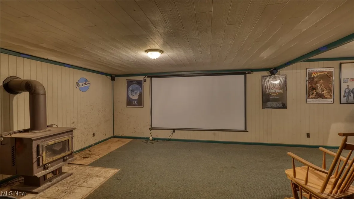 Carpeted cinema featuring a wood stove, wood ceiling, wooden walls, and baseboards