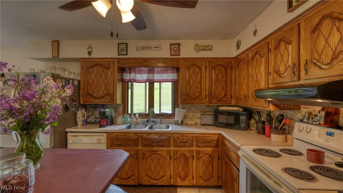 Kitchen with white appliances, a sink, under cabinet range hood, light countertops, and brown cabinetry