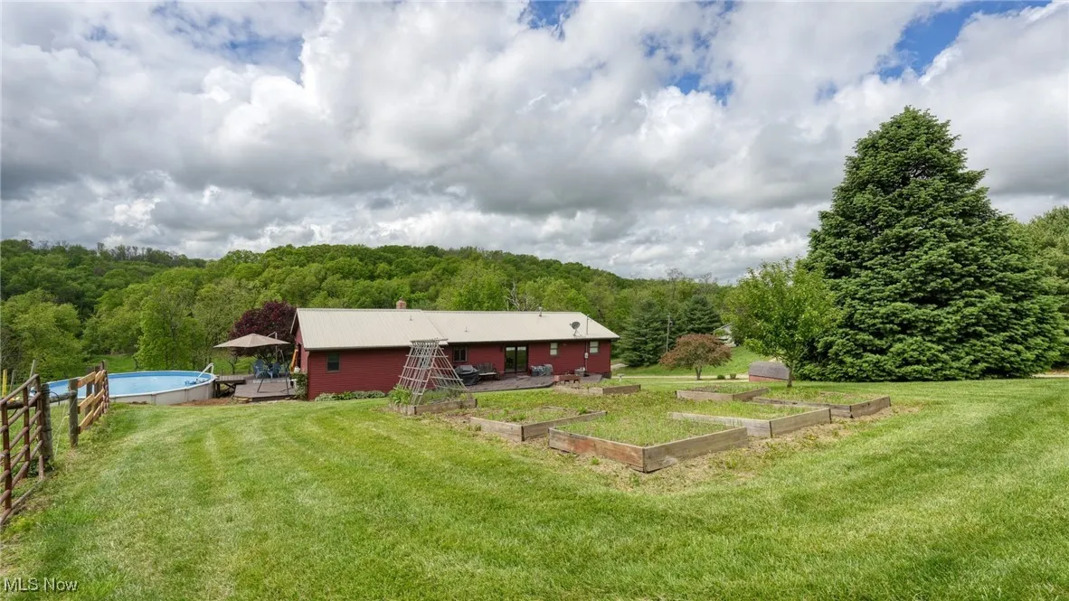 View of grassy yard featuring a vegetable garden, a forest view, and an outdoor pool